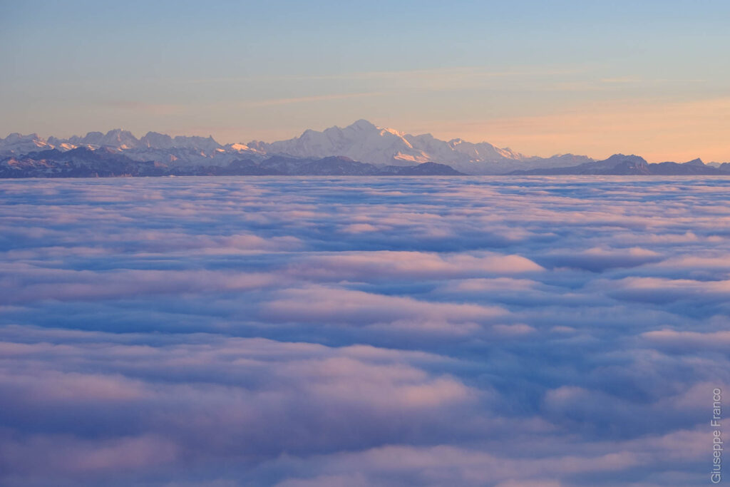 Switzerland is covered by clouds between the mountains. The sun is setting ans the Mont-Blanc is showing its grandeur.